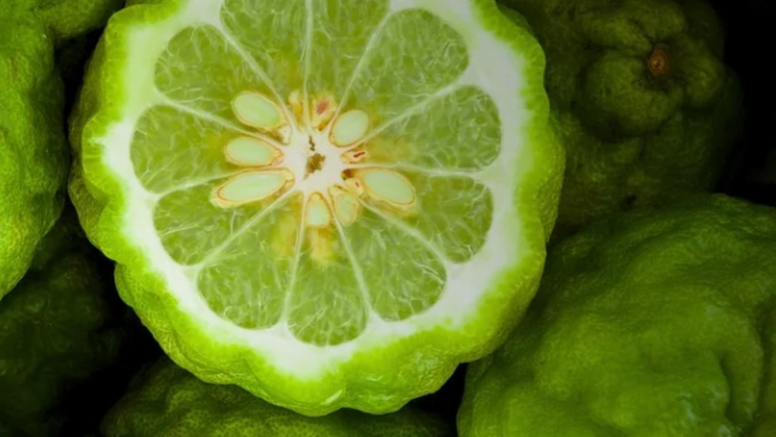 Close-up of green citrus fruit with a sliced fruit showing white interior.