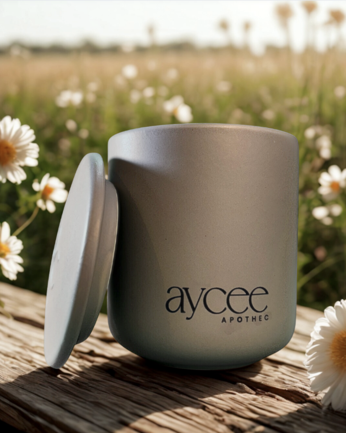 Gray Aycee Apothec ceramic container on a wooden surface with flowers in the background