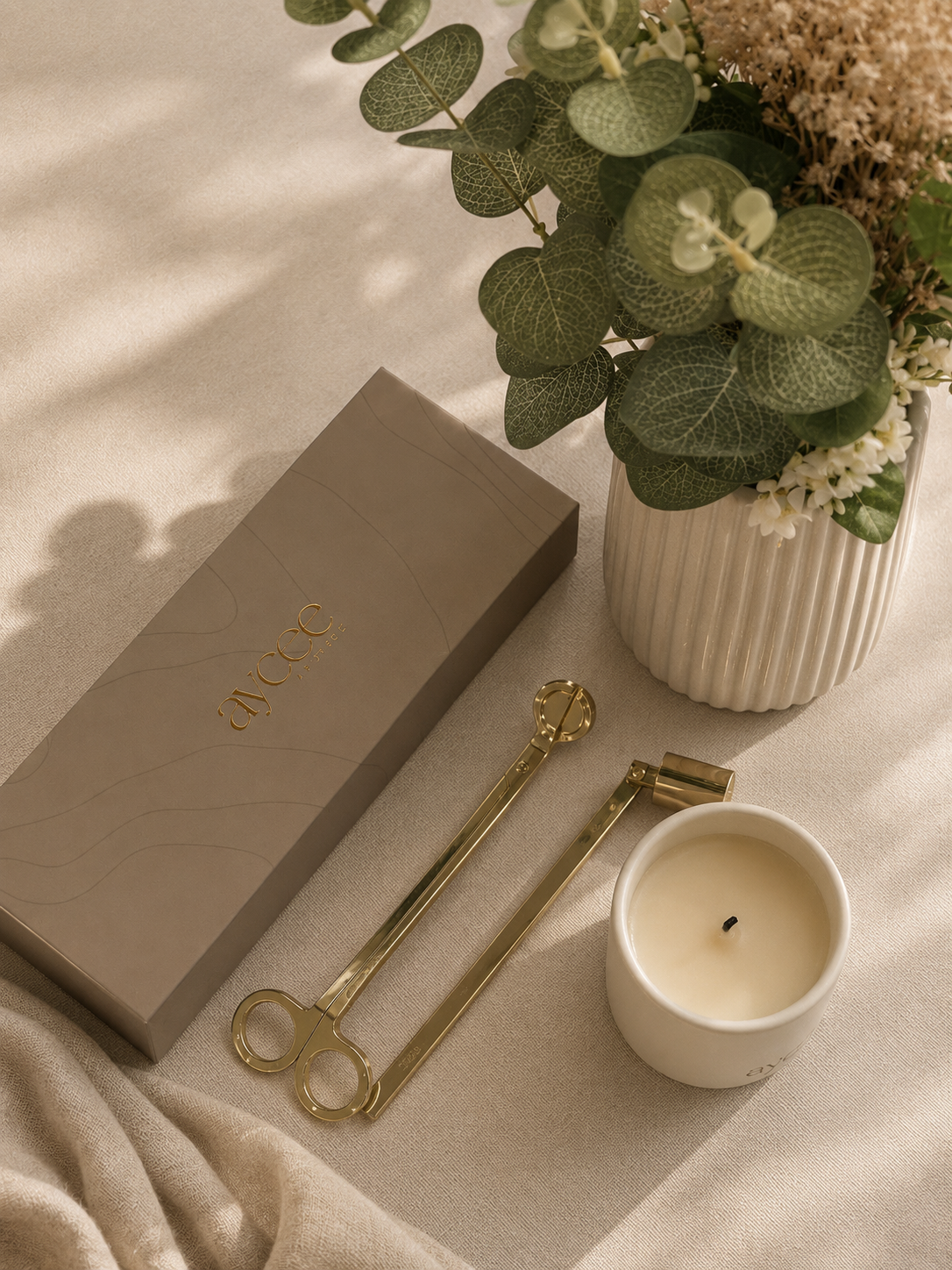 A candle with candle care set of tools on a linen tablecloth next to flowers