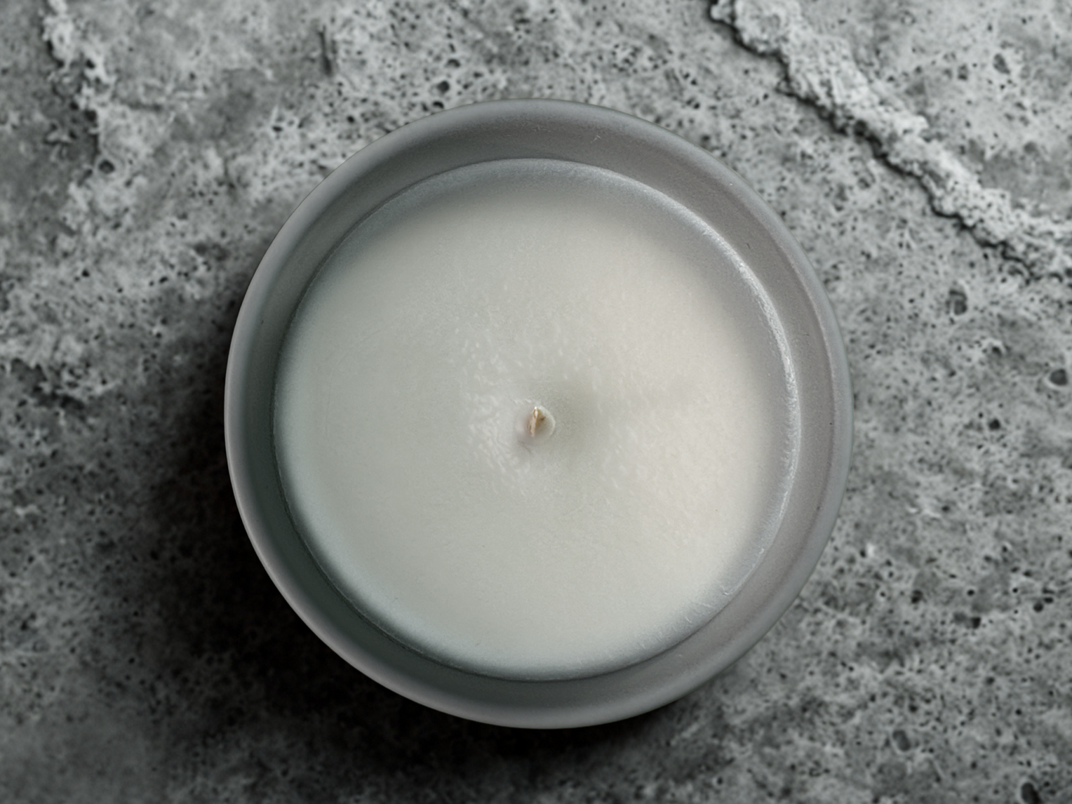 A grey ceramic candle jar pictured from above in close up on a textured grey surface