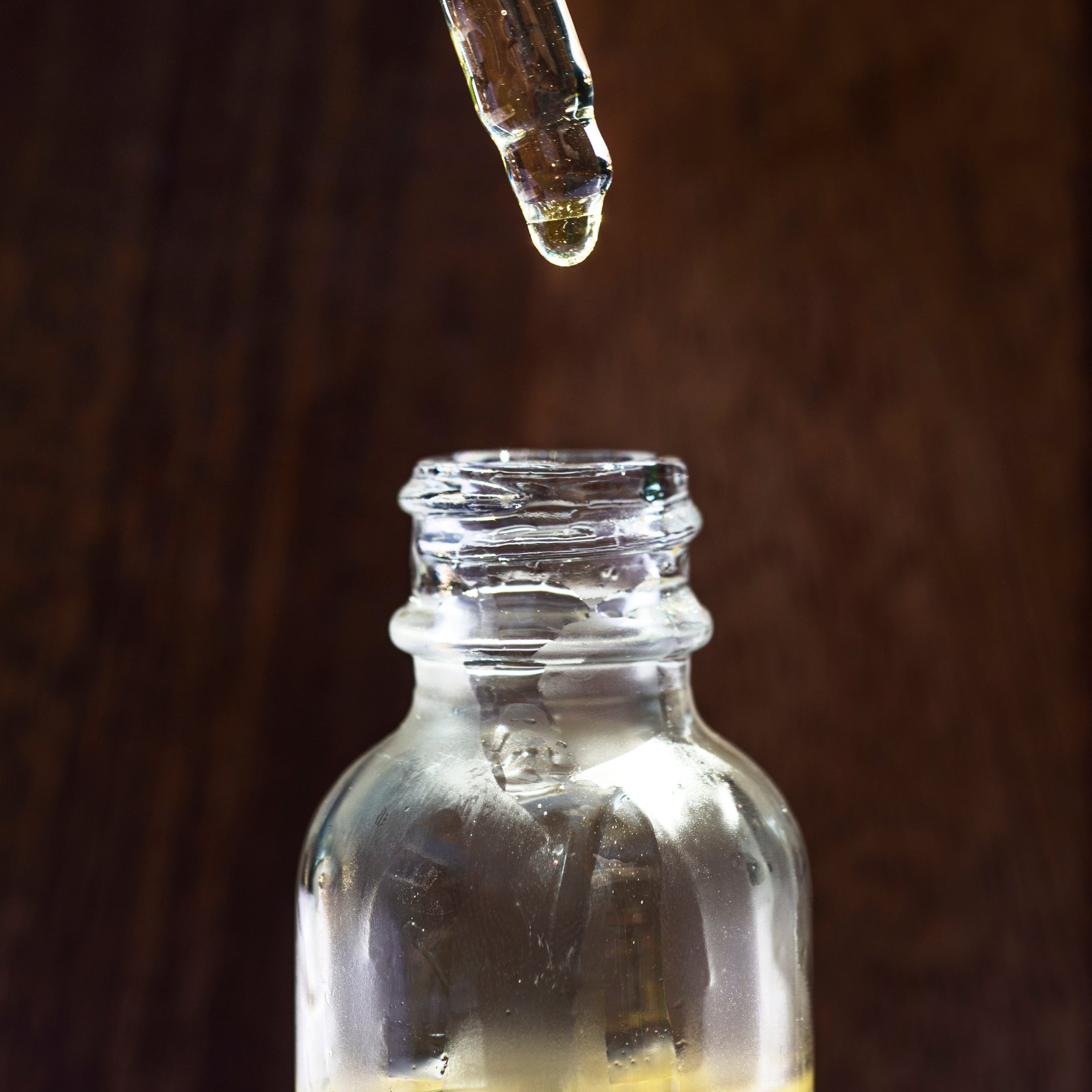 A small clear glass bottle of oil with a glass dropper dripping oil into it from above