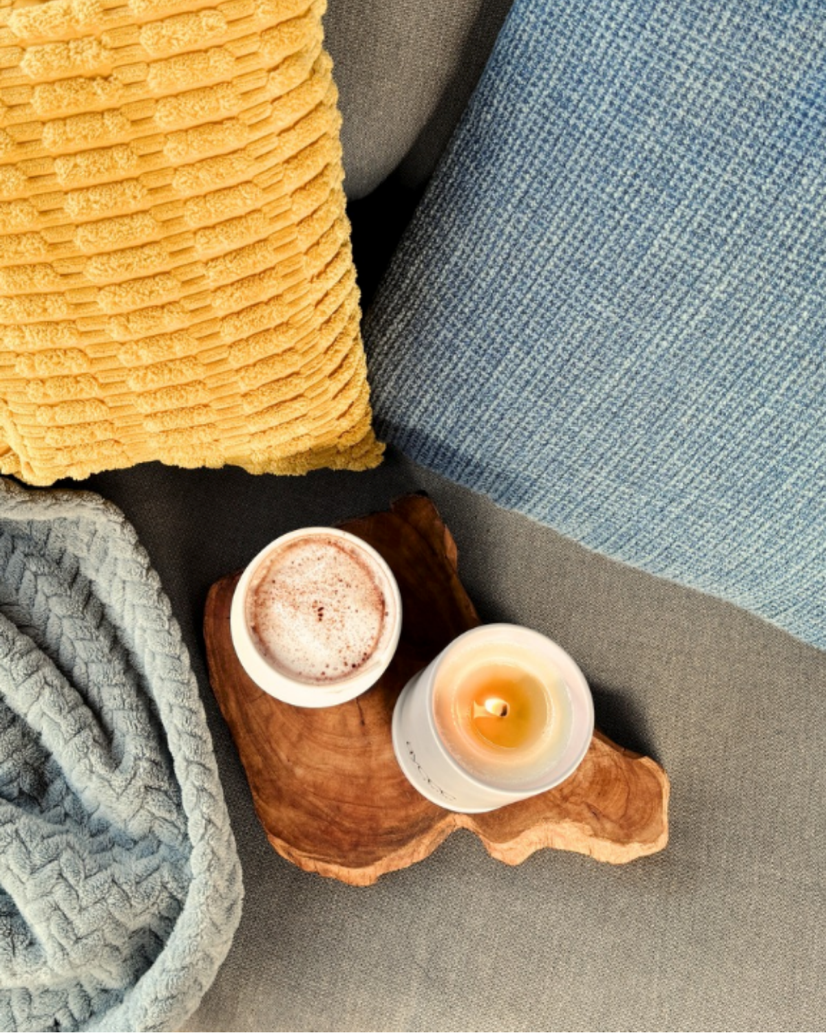 Candle on a wooden coaster with textured pillows and blanket on a sofa