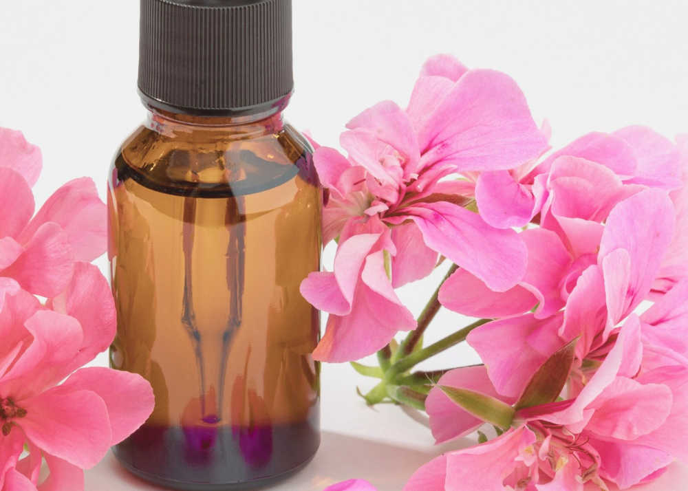 Amber glass dropper bottle with pink geranium flowers on a white background