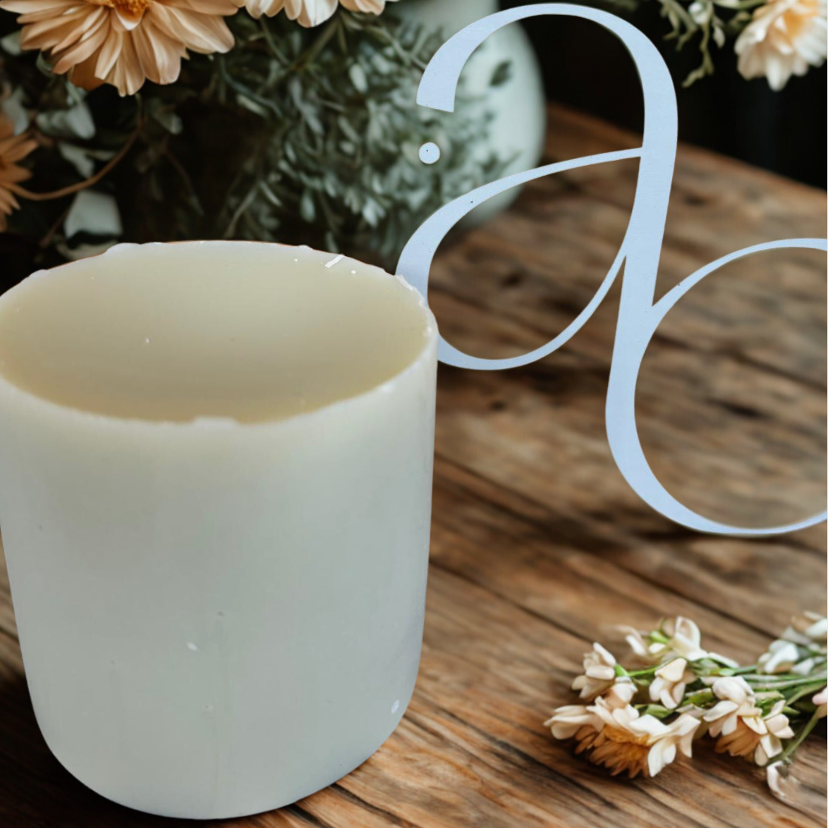 A wax candle on a table top with flowers behind and the AC logo