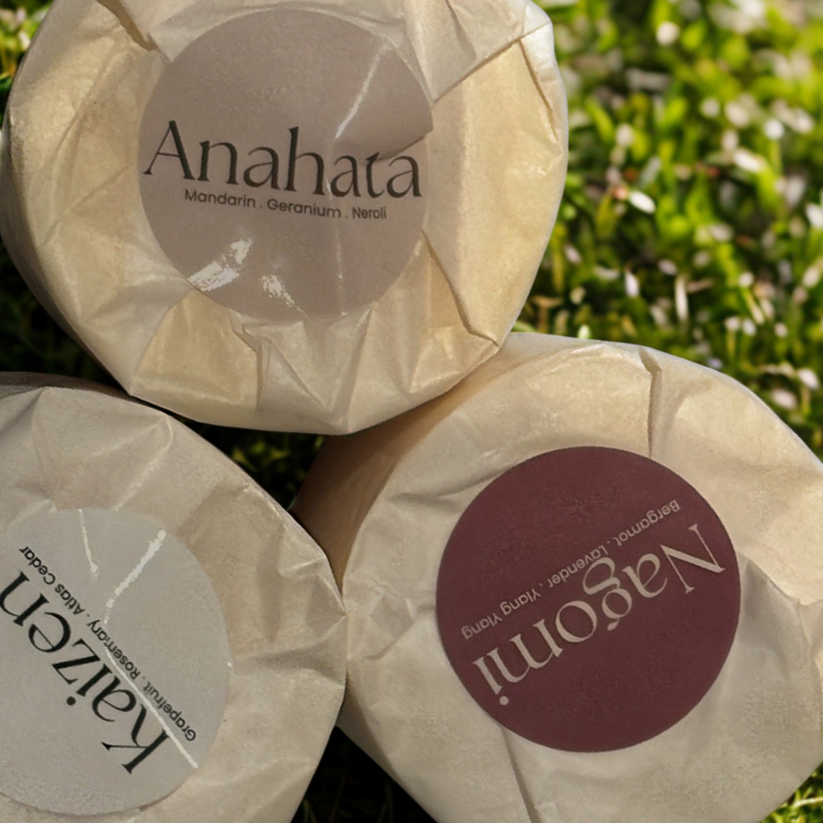 Three candles wrapped in tissue paper with labels on top resting on grass