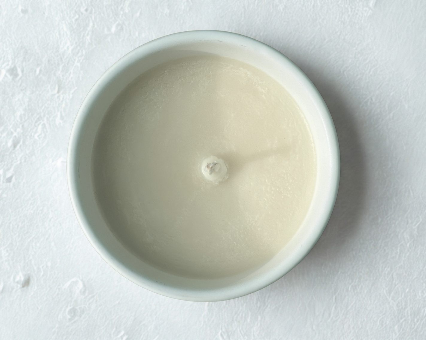 A white ceramic candle jar pictured from above in close up on a white surface