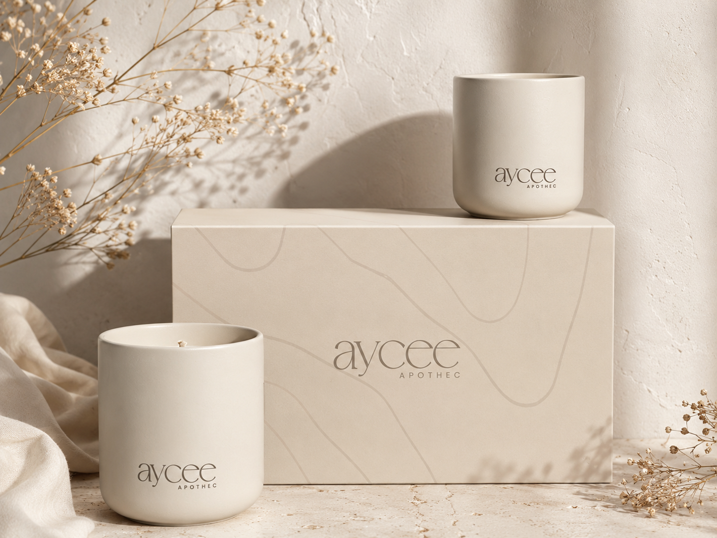 Two Aycee Apothec candles on a textured surface with a matching box in the background.